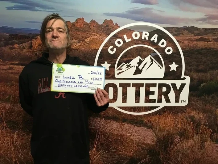LowellB.在科罗拉多彩票背景前，手持一张$1,000的大支票